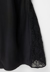 Schwarzes Kleid aus einem durchscheinenden Stoff mit einem zarten Spitzen-Seitenpaneel. Der Saum ist gewellt, was die Weichheit und Textur des Kleidungsstücks betont.