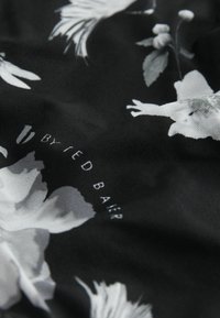 Schwarzer Stoff mit weißen Blumenmustern und teilweise sichtbarem Text "BY RED BALR", der darauf gedruckt ist.