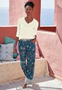 Light-colored long-sleeve top with a button detail, paired with dark blue patterned pants featuring floral designs and white lace accents.
