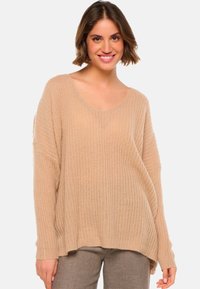 Pull en tricot beige surdimensionné avec un décolleté en V et une texture côtelée. Il présente des manches longues et un ourlet légèrement arrondi. Idéal pour le superposition.