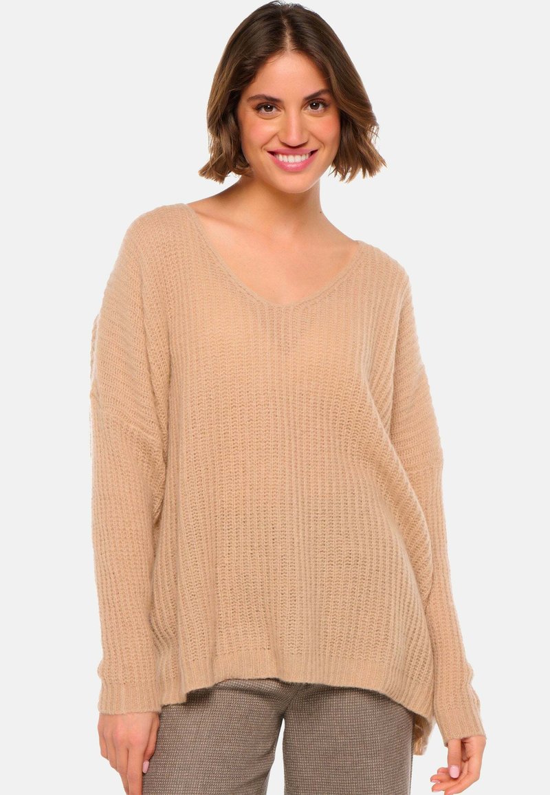 Pull en tricot beige surdimensionné avec un décolleté en V et une texture côtelée. Il présente des manches longues et un ourlet légèrement arrondi. Idéal pour le superposition.