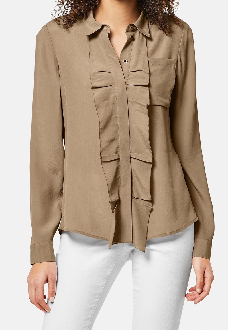 Blusa marrone a maniche lunghe con dettagli a volant sul davanti, chiusura con bottoni e un taschino sul petto; tessuto dalla consistenza liscia.