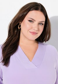 Top lilla chiaro con scollatura a V, texture liscia e maniche lunghe. Presenta orecchini a cerchio dorati come accessori.