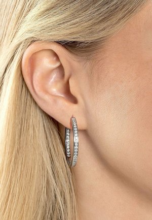 Boucles d'oreilles en argent en forme de créoles avec deux cercles entrelacés, mettant en évidence une rangée de petites pierres précieuses transparentes le long du bord extérieur.