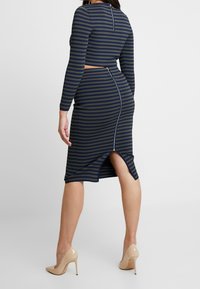 Two-piece outfit featuring a fitted striped crop top and matching mid-length skirt. Dark green and navy stripes, back zip closure, and high slit.