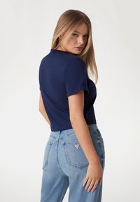 Marinblå cropped t-shirt med korta ärmar, i kombination med ljusblå högmidjade jeans med en lappl på bakfickan.