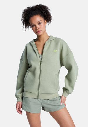 Felpa con cappuccio verde chiaro con zip, tessuto testurizzato, taglio oversize e tasche frontali. Presenta un piccolo logo in verde lime a contrasto.