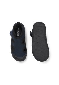 Marinblå vattenskor med svarta sulor, utrustade med utskurna detaljer, en kardborrerem och texturerade gummisulor för grepp och flexibilitet.