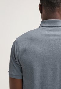 Grå polo-shirt med en strukturerad väv, korta ärmar och en vikbar krage, visad bakifrån utan synliga logos eller detaljer.