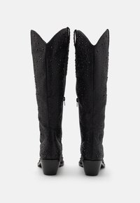 Botas negras hasta la rodilla con puntas afiladas, exterior texturizado con detalles de remaches y tacones apilados. Cierres de cremallera en los laterales.