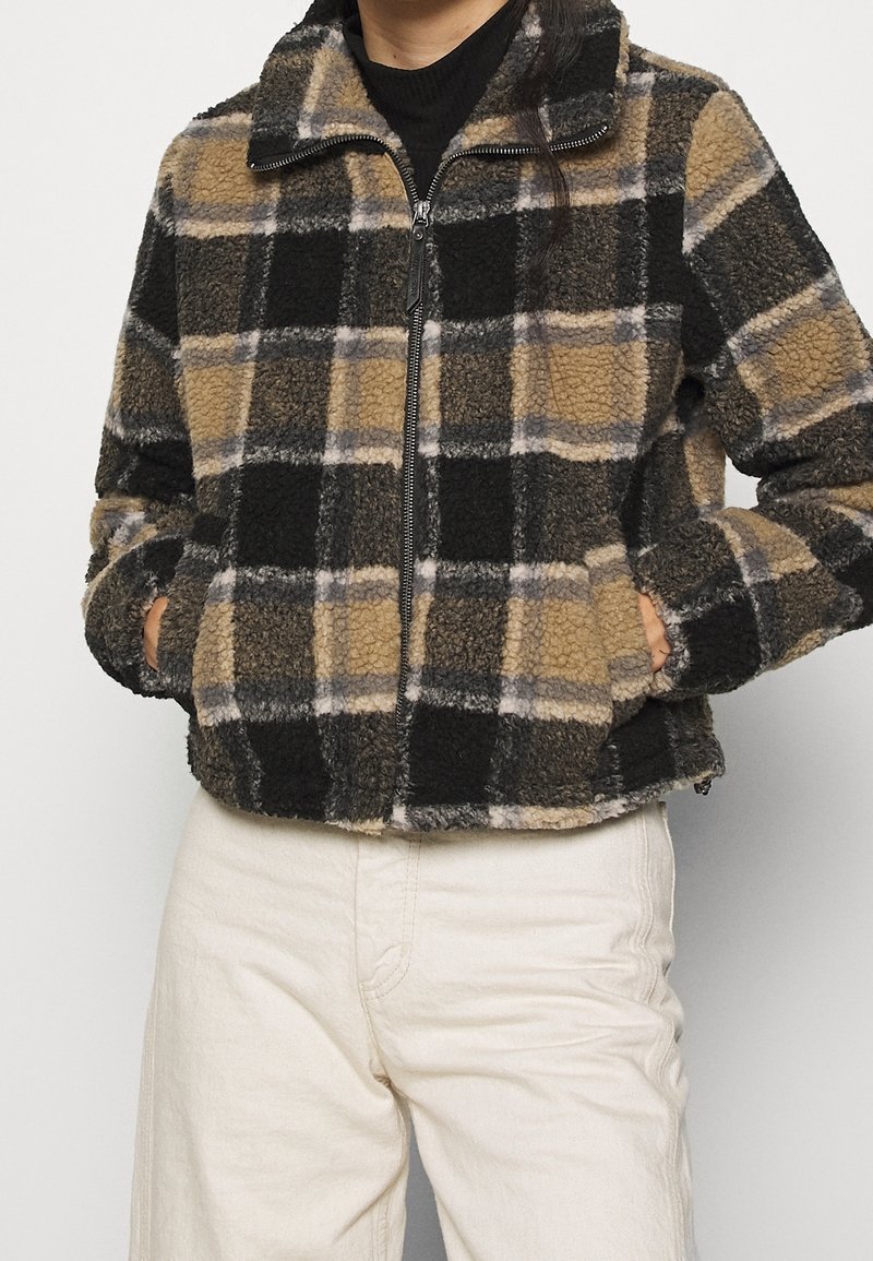 Chaqueta de forro polar con un patrón de cuadros en negro, marrón y gris, que cuenta con un cierre central de cremallera, bolsillos laterales y un cuello. Superficie texturada.