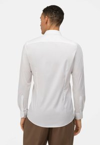 Witte blouse met lange mouwen en een puntige kraag, met een gladde textuur, knoopmanchetten en een gebogen zoom, gezien vanachter.