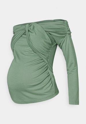 Haut vert à épaules dénudées en tissu doux. Présente des détails froncés et une manche longue d'un côté, créant un design asymétrique.
