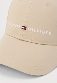 Beige Tommy Hilfiger baseball sapka, hímezett márkanevével és kis piros, fehér és tengerészkék téglalap alakú logójával az elülső panelen.