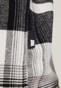 Zwart-wit geruit stof met verschillende streeptexturen; bevat een klein zwart-wit merklabel aan de rand.