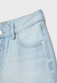 Jean en denim bleu clair montrant la poche avant, la boucle de ceinture et les détails des rivets métalliques sur un fond blanc uni.