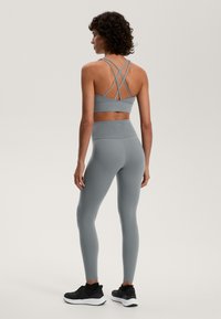 Siv športni modrček s prečnimi naramnicami in visokimi usklajenimi leggins. Gladka tekstura, prilegajoč dizajn, v kombinaciji s črnimi atletski čevlji.