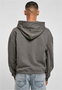 Sudadera con capucha gris de corte relajado y puños de canalé, vista desde la parte de atrás, combinada con jeans azules ligeramente desgastados.