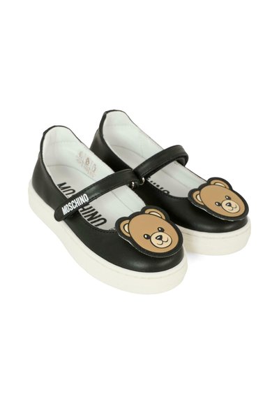 Scarpe in pelle nera con suola in gomma bianca, caratterizzate da un motivo a orsacchiotto sulla punta e una cintura sicura sulla parte superiore.