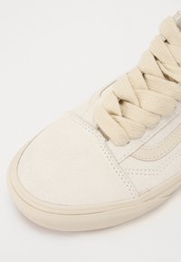 Beige nubuk sneaker krémszínű fűzőkkel, lapos orrésszel és texturált gumitalppal. Egyszerű dizájnja és kontrasztos oldalsávja jellemzi.
