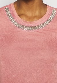 Rosafarbenes Sweatshirt mit Rundhalsausschnitt, das einen mit Silber verzierten Kragen und einen weichen, strukturierten Stoff aufweist.
