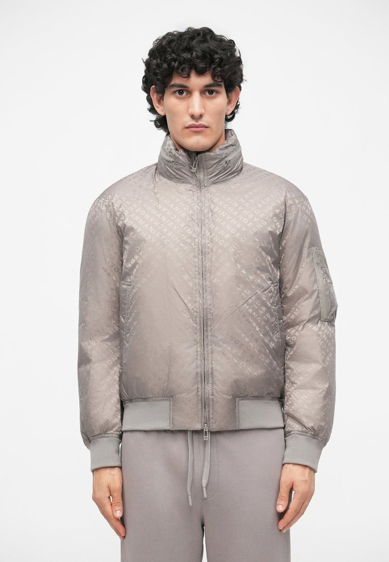 Jachetă bomber gri cu o textură matlasată și un model subtil cu logo. Dispune de guler în picioare, închidere cu fermoar și mansete ribbed.