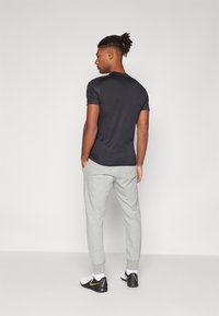 T-shirt nera a maniche corte abbinata a jogging leggeri grigi e scarpe da ginnastica nere con un accento dorato. Modello mostrato da dietro.