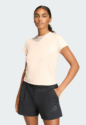 Jasnoróżowa sportowa koszulka z krótkimi rękawami, okrągłym dekoltem i subtelnym logo. W zestawie z czarnymi szortami z bocznymi kieszeniami.
