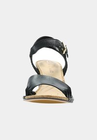 Sandale en cuir noir avec une large lanière, un dessus texturé et une semelle en liège. Lanière de cheville ajustable avec une boucle métallique.