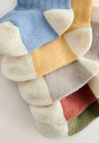 Stapeltje van vijf enkelsokken in blauw, geel, beige, roestkleur en olijfgroen met crèmekleurige accenten op de tenen en hielen.