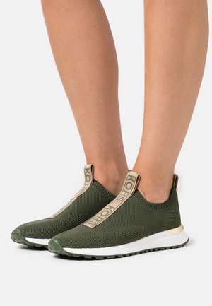 Groene gebreide instap sneakers hebben een tan logo-band, een gestructureerde bovenkant en een witte rubberen zool met groene accenten.
