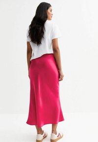 Satijnen roze midi-jurk met een vloeiende silhouet, gecombineerd met een relaxte witte t-shirt en casual witte schoenen met gekleurde accenten.