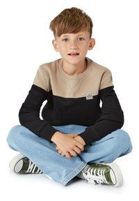 Beige och svart färgblockerad sweatshirt med ribbade muddar, med en logotyp patch. Kombinerad med ljusblå jeans och gröna sneakers.