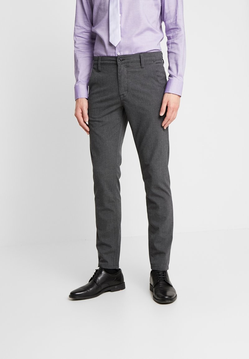 Šedé slim fit kalhoty z texturované látky s plochým předním designem, doplněné o černé boty a světle fialovou košili s kravatou.