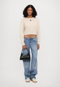 Felpa beige corta con una toppa con logo, abbinata a jeans a gamba larga blu chiaro con un motivo grafico. Borsa in finta pelle di coccodrillo nera.
