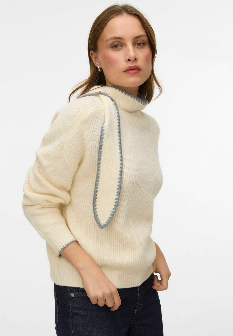 Krēmkrāsas džemperis ar augstu apkakli un pelēkiem ribotiem elementiem. Mīksta tekstūra un brīvs pieguļošs siluets ar nolaistām plecu līnijām.