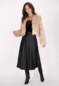 Beige nepbont cropped jack over een zwarte satijnen slipdress. Zwarte kniehoge haklaarzen. Zachte textuur en elegante silhouet.