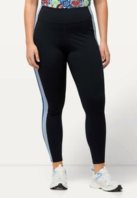 Svarta leggings med ljusblå sidestreck, tillverkade av elastiskt material. Bärs med vita sneakers med blå detaljer.