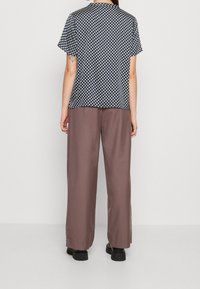 Top corto a maniche corte con motivo bianco e nero abbinato a pantaloni larghi marroni, che mostrano una vestibilità rilassata e un design minimalista.