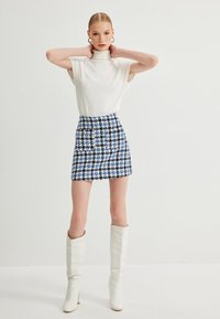 Witte geribde top met korte mouwen, blauw-witte houndstooth minirok en kniekorte witte hoge hakken. Zachte textuur, elegant ontwerp.