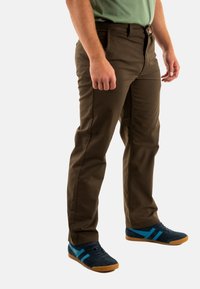 Pantaloni marroni con un design a gamba dritta, realizzati in materiale resistente, dotati di zip e cintura. Indossati con sneakers blu marino con accenti turchesi.