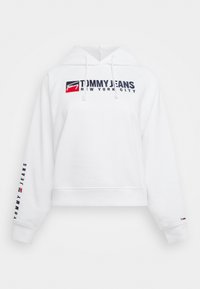 Sudadera blanca con el logotipo "Tommy Jeans New York City" en el pecho, texto "Tommy Jeans" en la manga izquierda y pequeña bandera en el puño derecho.