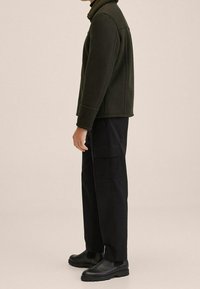 Giacca in pile verde oliva con colletto alto, abbinata a pantaloni cargo neri e stivali neri alla caviglia. Design semplice e utilitario senza motivi.
