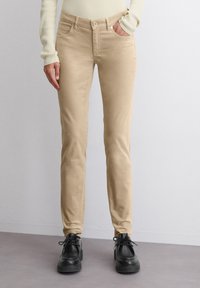 Beige puuvillasegupüksid slim fit lõikega, viie taskuga ja nupuga sulgemine. Kombineeritud mustade nööbist kingadega.