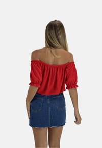 Rode off-the-shoulder top met pofmouwen, gecombineerd met een hoog-genoemde denim mini rok met een rafelende zoom en achterzakken.