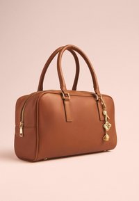 Sac à main en cuir marron avec des anses arrondies, une fermeture éclair, des accessoires en or et un charm décoratif avec des accents floraux.