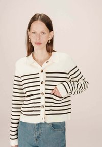 Cardigan rayé en crème et marron, avec un col, une fermeture à boutons et deux poches avant. Tissu tricoté doux et texturé.