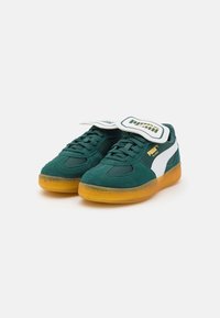 Zielone zamszowe sneakersy z białymi akcentami, z wyściełanym językiem i gumową podeszwą. Oferują teksturowaną cholewkę oraz sznurowany design.