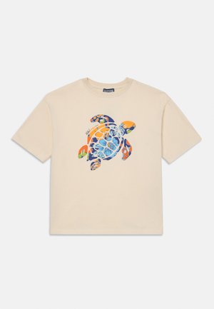 T-shirt bege de manga curta com um gráfico colorido de tartaruga marinha, apresentando padrões florais em azul, laranja e verde na parte da frente.
