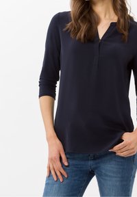 Haut à manches longues bleu marine avec un col henley, doté d'une patte de boutonnage et d'une texture douce et lisse. Associé à un jean en denim bleu clair.